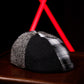 A black and gray plaid flat cap resting on a dark wooden surface with a black background and red geometric light beams behind it.