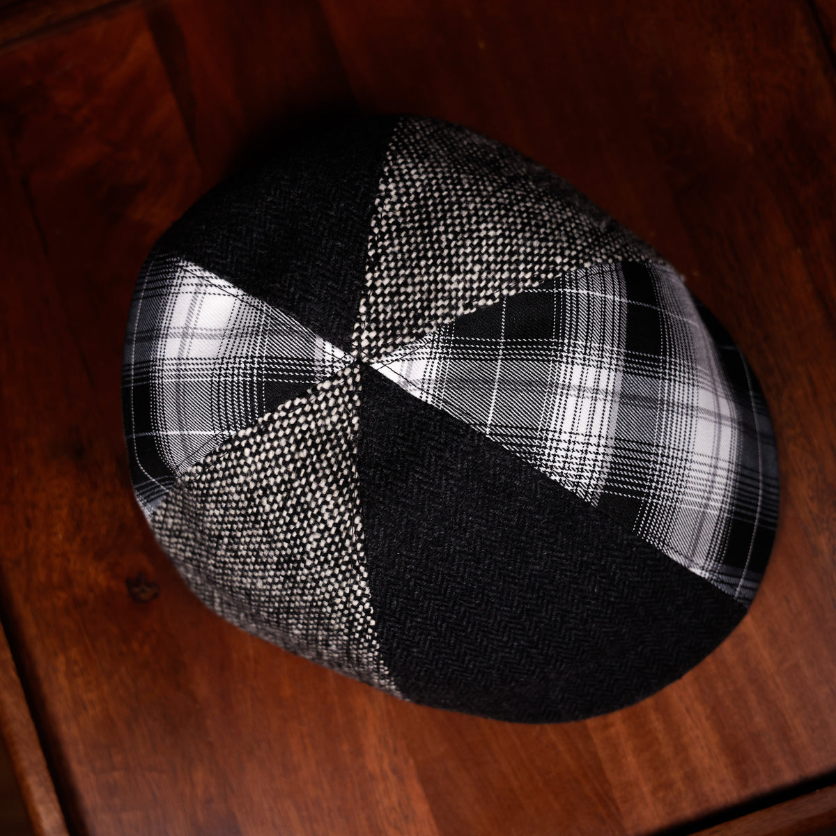 A black and white plaid and herringbone patterned skullcap resting on a dark brown wooden surface.