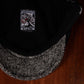 Close-up of a black trucker-style cap with a textured black-and-white brim, resting on a dark wooden surface. The inside of the crown features a black fabric lining with a rectangular embroidered patch showing a grim reaper and the text 'FUCK BEARZ' and 'REAPER OF THE DEAD'.