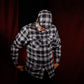 A man wearing a black and white plaid button-up shirt with matching plaid baseball cap, posed against a dark red curtain background.