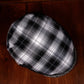 A black and white plaid flat cap resting on a dark wooden surface.