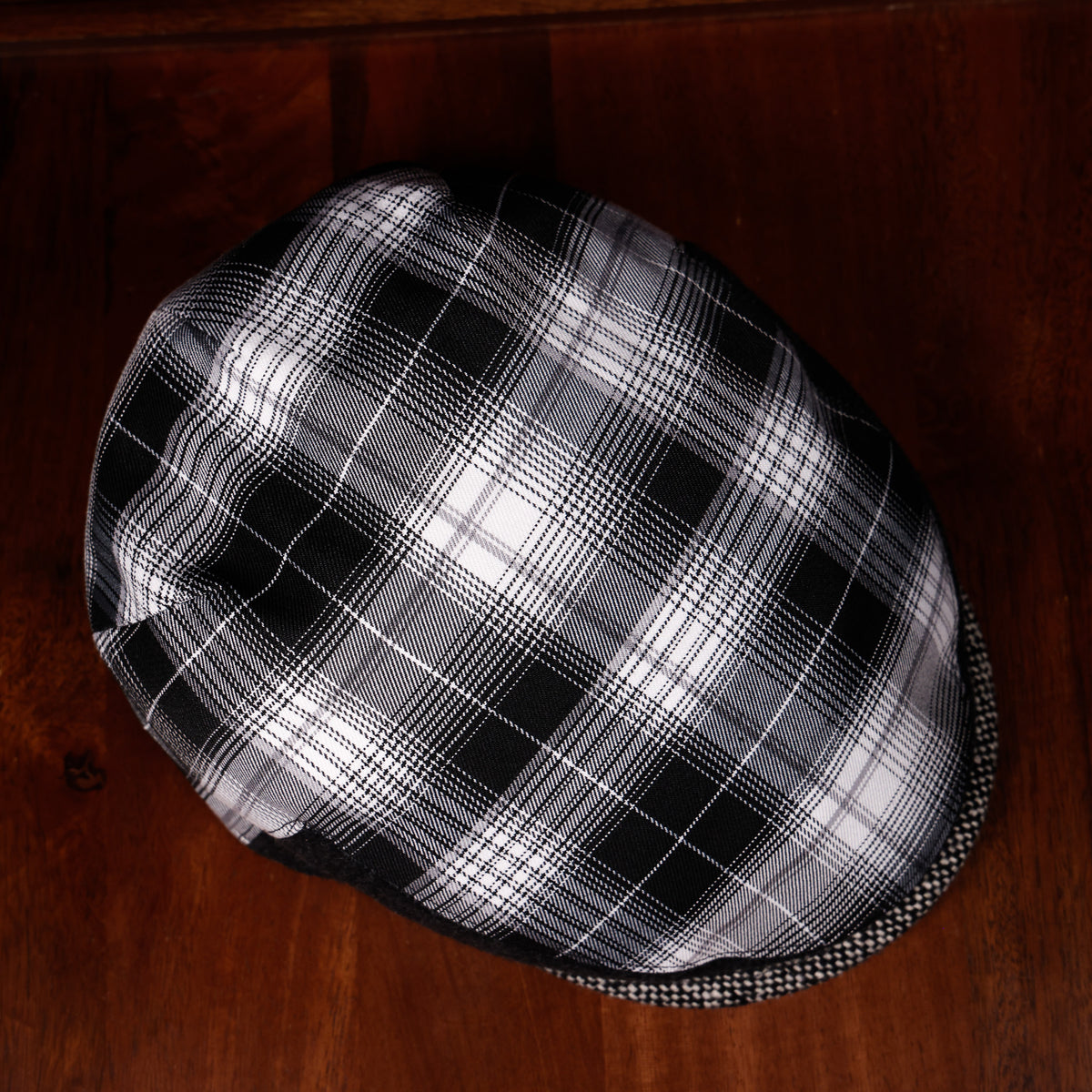 A black and white plaid flat cap resting on a dark wooden surface.