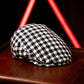 A black and white houndstooth patterned flat cap resting on a dark wooden surface, with a blurred red neon light in the background.