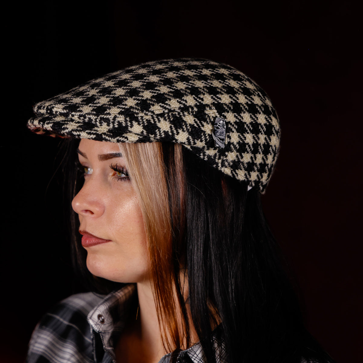 A woman in profile wearing a black and beige houndstooth flat cap against a dark background.