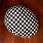 A top view of a black and white houndstooth patterned flat cap resting on a dark wooden surface.