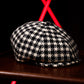 A black and white houndstooth flat cap resting on a dark wooden surface, with a blurred black background and bright red geometric light accents behind it.