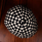 A black and cream houndstooth knit cap photographed from above on a dark brown wooden surface.