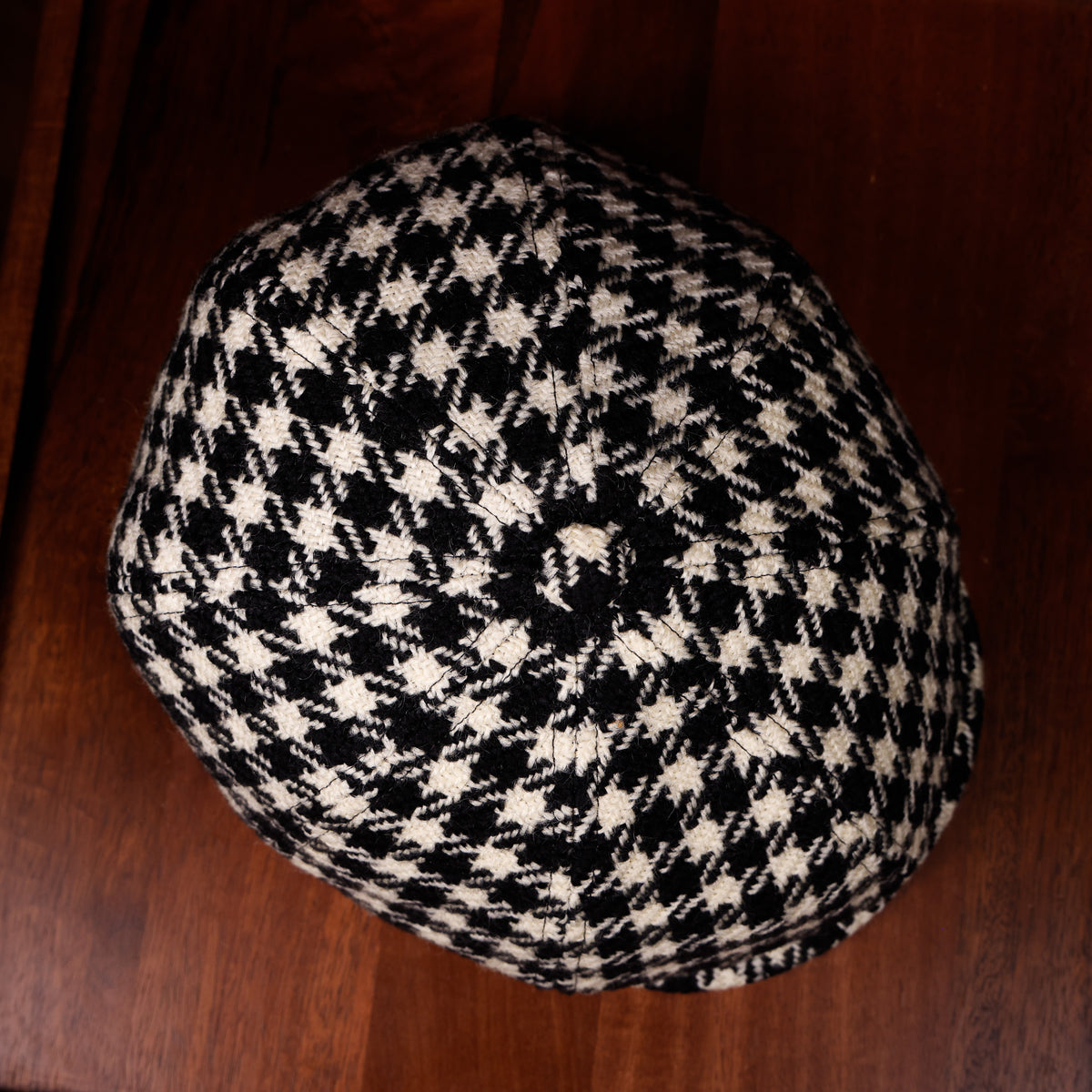 A black and cream houndstooth knit cap photographed from above on a dark brown wooden surface.