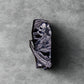 A coffin-shaped lighter with a detailed grim reaper design, featuring a metallic silver and black finish, set against a textured gray background.