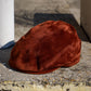 A rust-brown suede flat cap resting on a weathered concrete ledge outdoors.