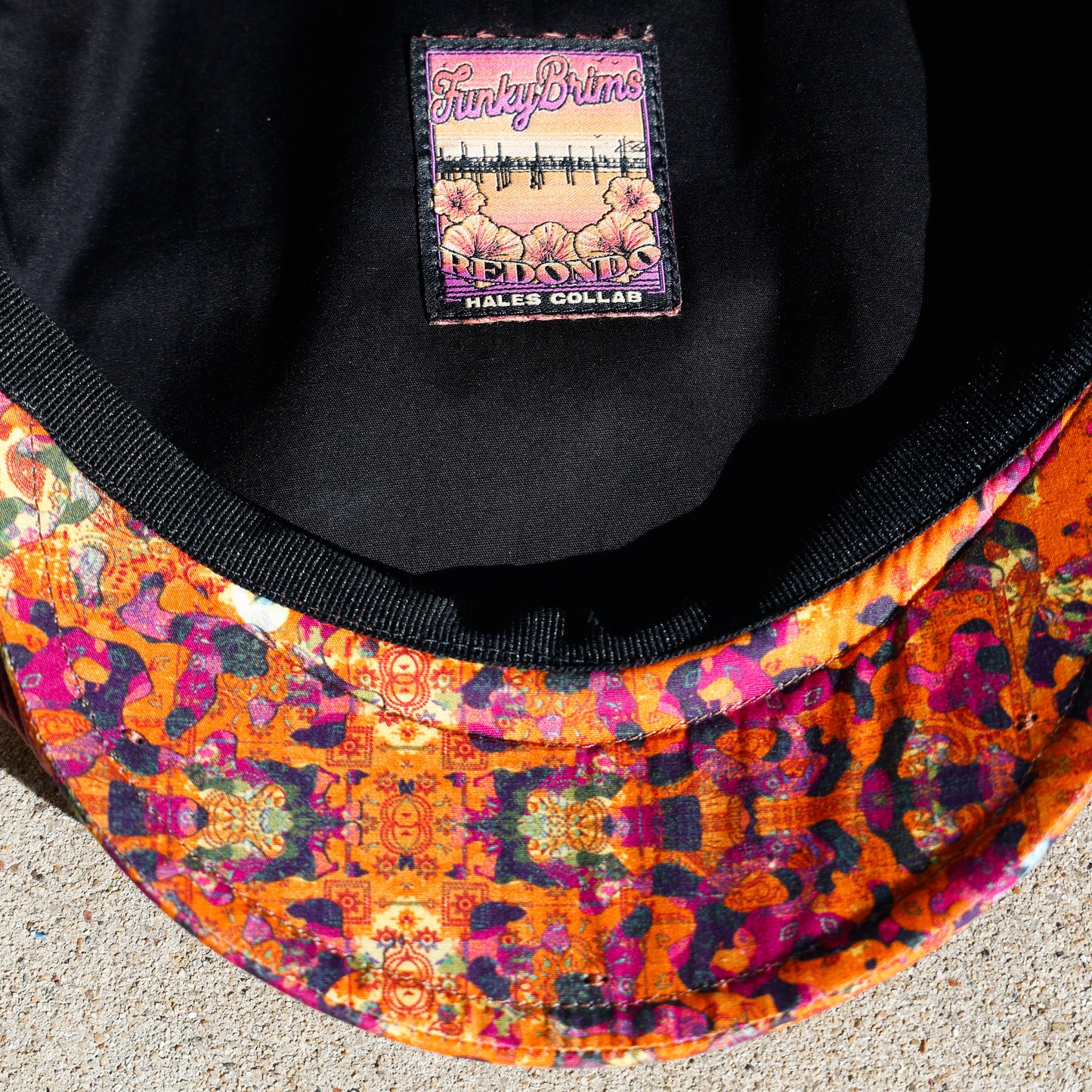 Close-up of a black baseball cap interior with a colorful patterned visor and a visible sewn-in label reading 'Funky Bricks' and 'Piano'.