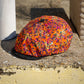A multicolor leopard-print flat cap with a black brim, resting on a weathered concrete ledge outdoors.