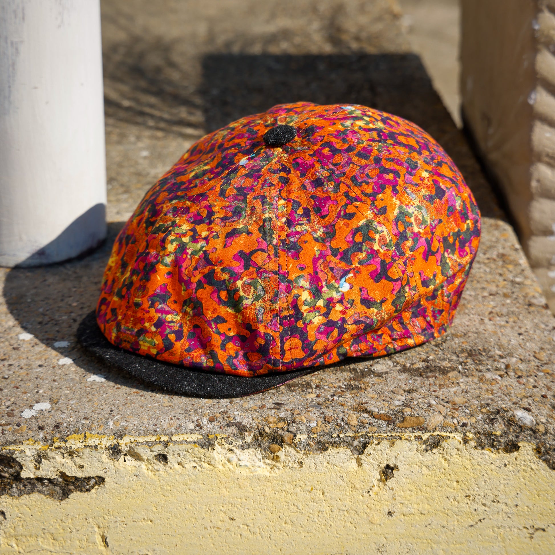 A multicolor leopard-print flat cap with a black brim, resting on a weathered concrete ledge outdoors.