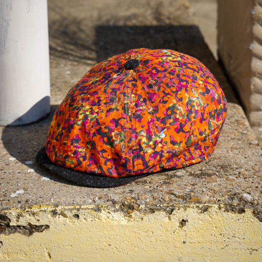 A multicolor leopard-print flat cap with a black brim, resting on a weathered concrete ledge outdoors.