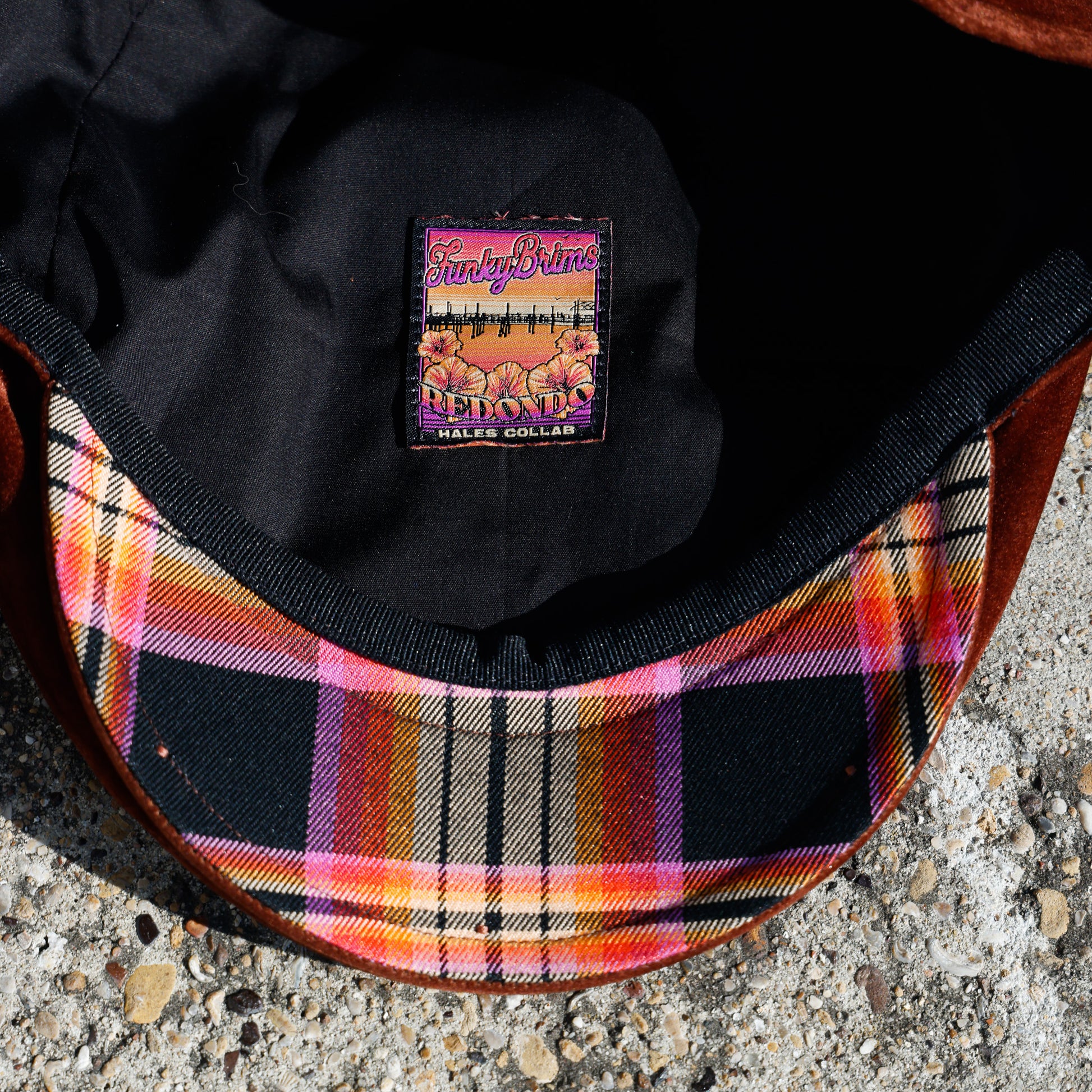 Close-up of the inside of a cap showing a colorful plaid lining with pink, orange, yellow, black, and white stripes, a black interior, and a sewn-on brand patch reading 'Sunny Days' and 'HALE SOLAR'.