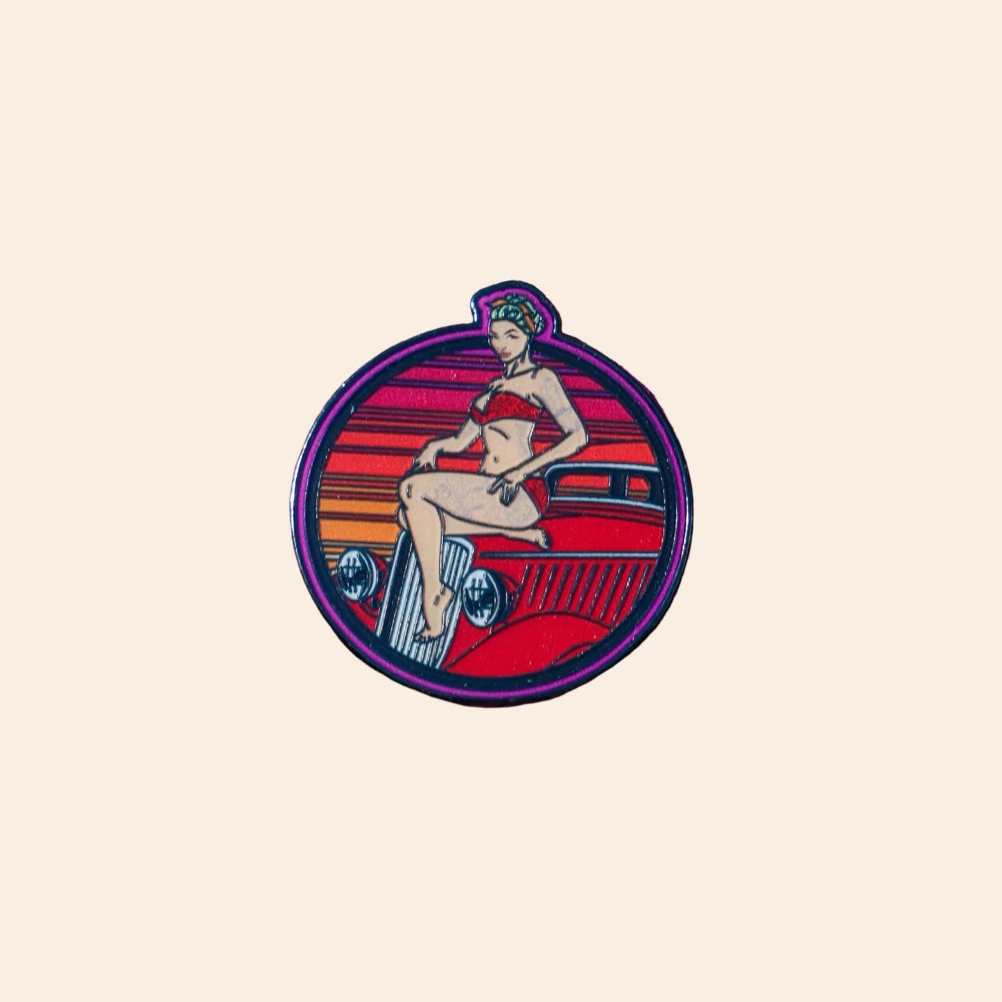 A circular enamel pin featuring a retro pin-up illustration of a woman sitting on a red car against an eggshell background.