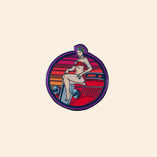 A circular enamel pin featuring a retro pin-up illustration of a woman sitting on a red car against an eggshell background.