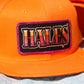 Close-up of a bright orange baseball cap featuring a rectangular embroidered patch with the word 'HALES' in stylized multicolor lettering on a black background with a purple border.