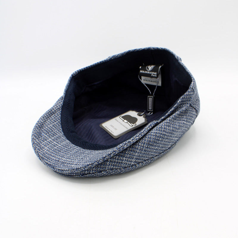 A blue and gray herringbone tweed flat cap with a dark navy blue interior, shown on a clean white background with its retail tags visible.