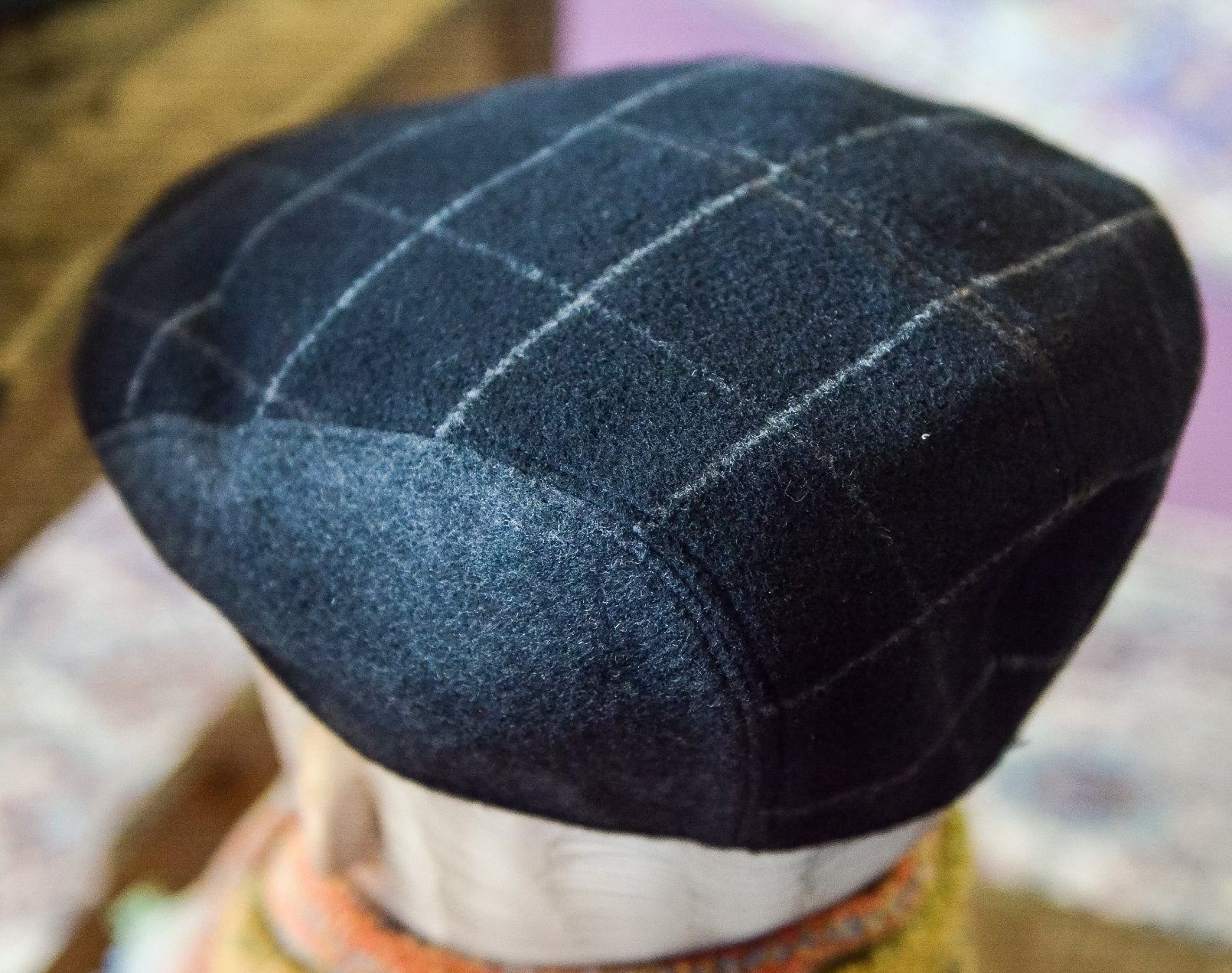 A close-up of a dark navy blue wool flat cap with a white windowpane plaid pattern, displayed on a mannequin head.