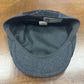 A dark gray wool flat cap with a black fleece interior, shown from the inside on a wooden desk. The brand label reads 'FunkyBrims.