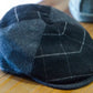 A dark charcoal gray wool flat cap with a subtle windowpane plaid pattern, resting on a wooden tabletop.