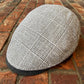 A gray and white plaid flat cap resting on a red brick surface.