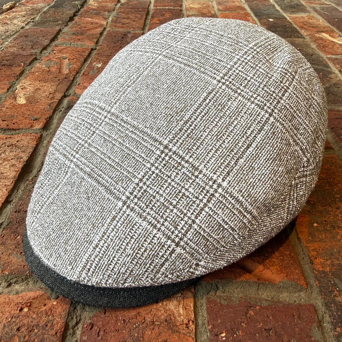 A gray and white plaid flat cap resting on a red brick surface.
