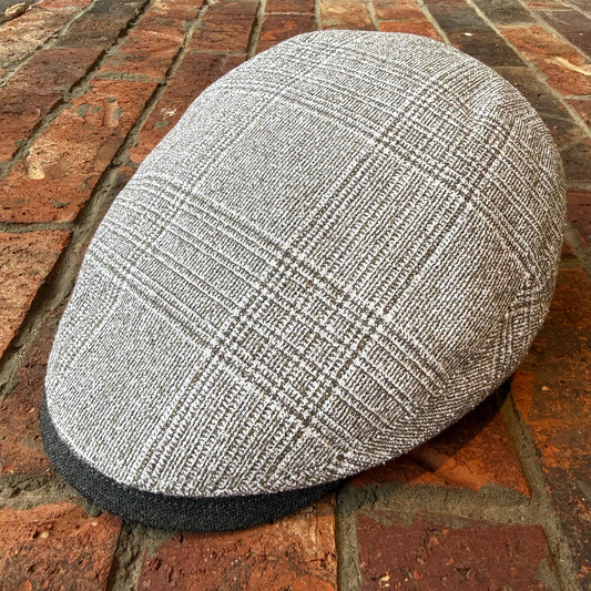 A gray and white plaid flat cap resting on a red brick surface.