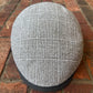 A gray and white plaid flat cap resting on a red brick surface.