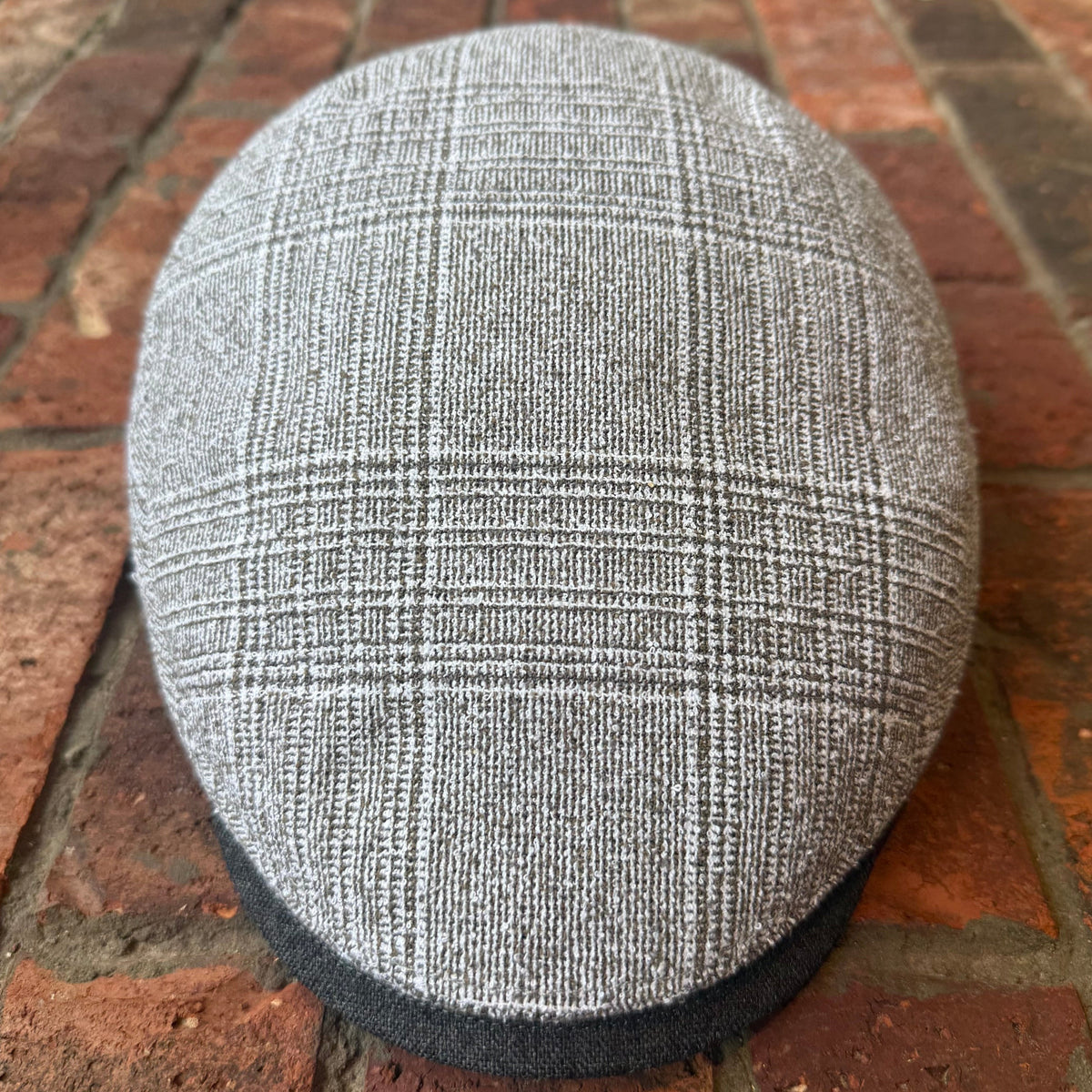 A gray and white plaid flat cap resting on a red brick surface.
