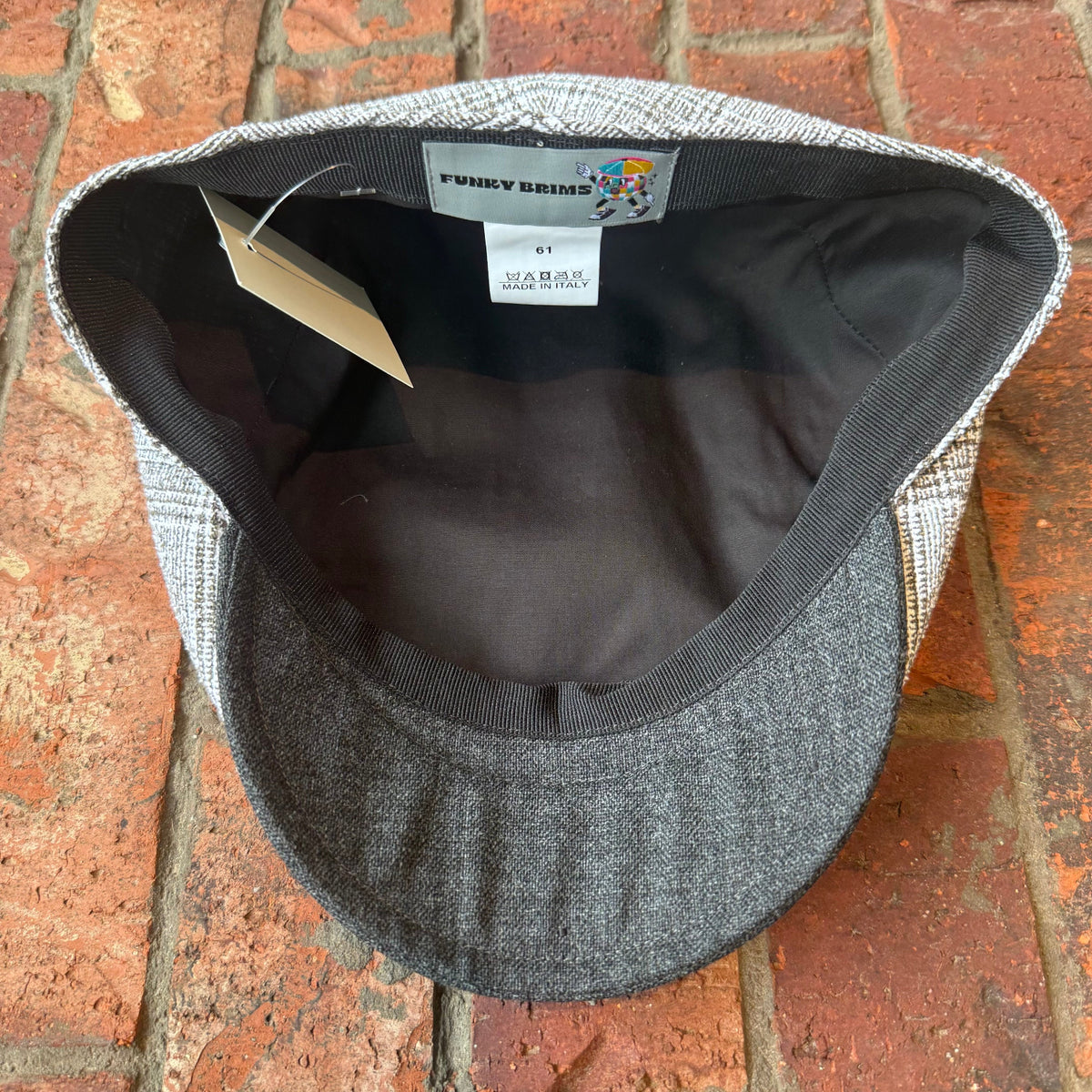 A gray and black tweed flat cap with a dark gray ribbed visor and black interior, photographed from above on a red brick surface. The brand label reads 'FUNKYBRIMS'.