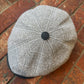 A gray and white plaid flat cap with a black button on top, resting on a red brick surface.