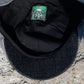 Close-up of the inside of a black baseball cap, showing a black fabric brim, black interior lining, and a square green-and-black patch with a stylized face graphic.