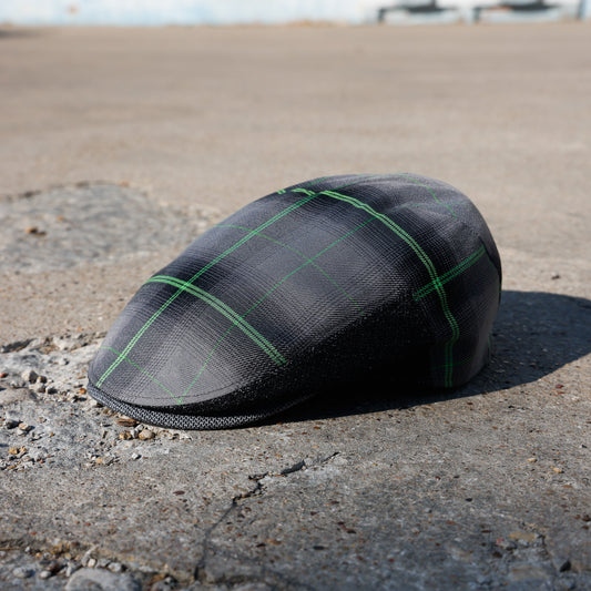 A black textured flat cap with a green plaid pattern, resting on a concrete surface outdoors.