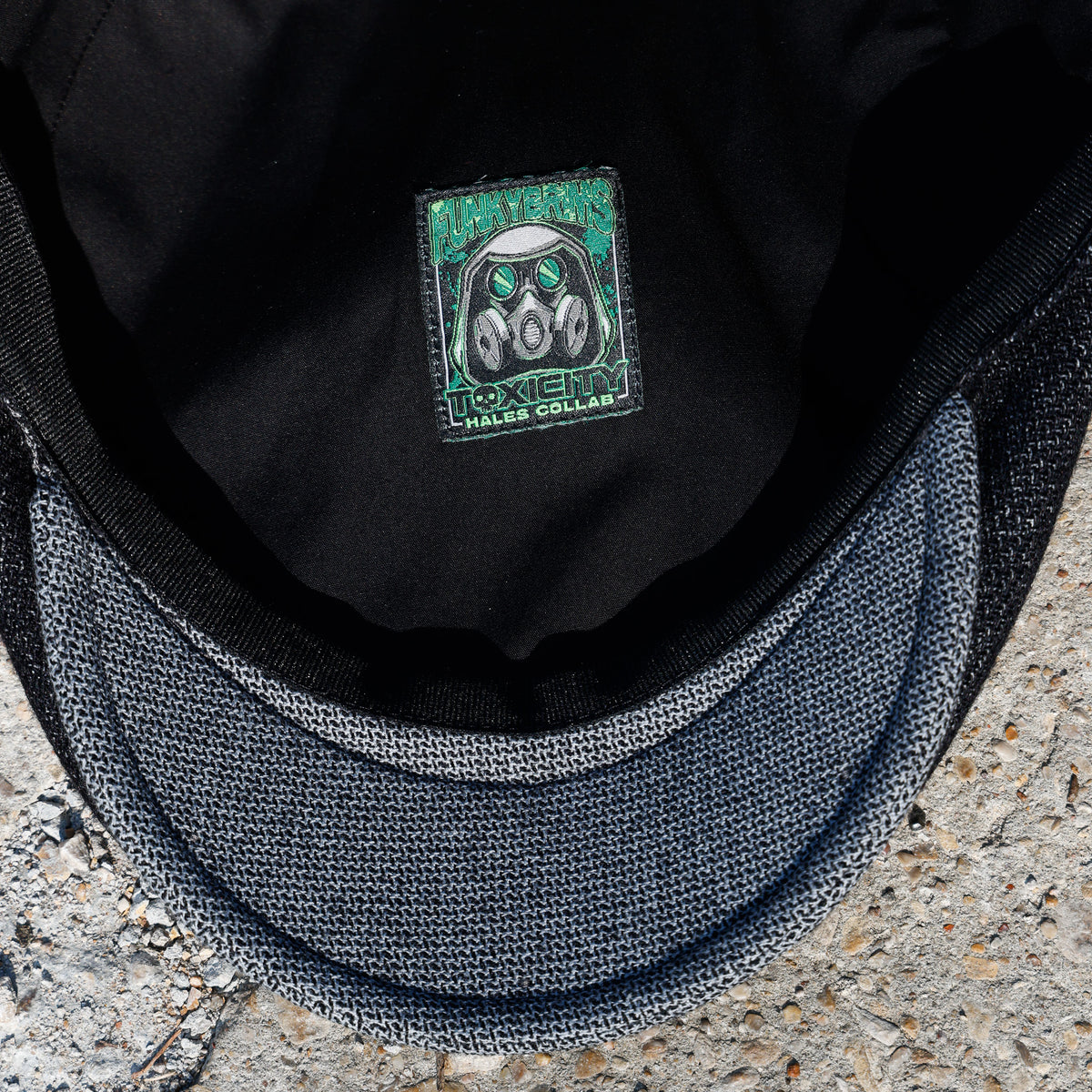 Close-up of the inside of a black cap showing a square embroidered patch with a gas mask design and the text 'TOXIC HAZARDS COLLAR'.