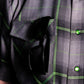Close-up of a person wearing a dark gray plaid shirt with bright green lines and shiny green buttons, with black sunglasses tucked into the chest pocket.