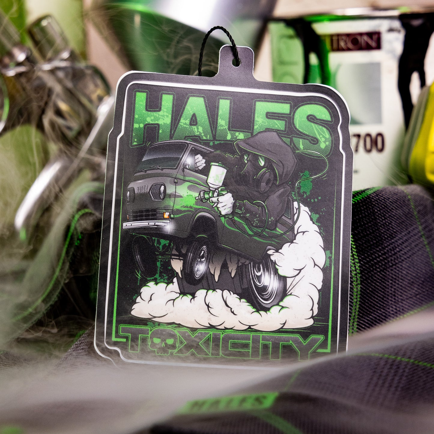 A rectangular Hales Toxic City car air freshener tag featuring a green and black graphic of a skull driving a van with smoke, shown hanging in a product display.
