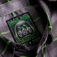 Close-up of a dark gray and black plaid button-down shirt with bright green stripes, featuring a sewn-in embroidered patch with a gas mask graphic and the text 'HALES TOXICITY DESIGNED IN TEXAS'.