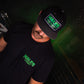A man wearing a black t-shirt and a black baseball cap, both featuring a green and white 'HALES TOXICITY' graphic print, in a dark, moody setting with green ambient lighting.