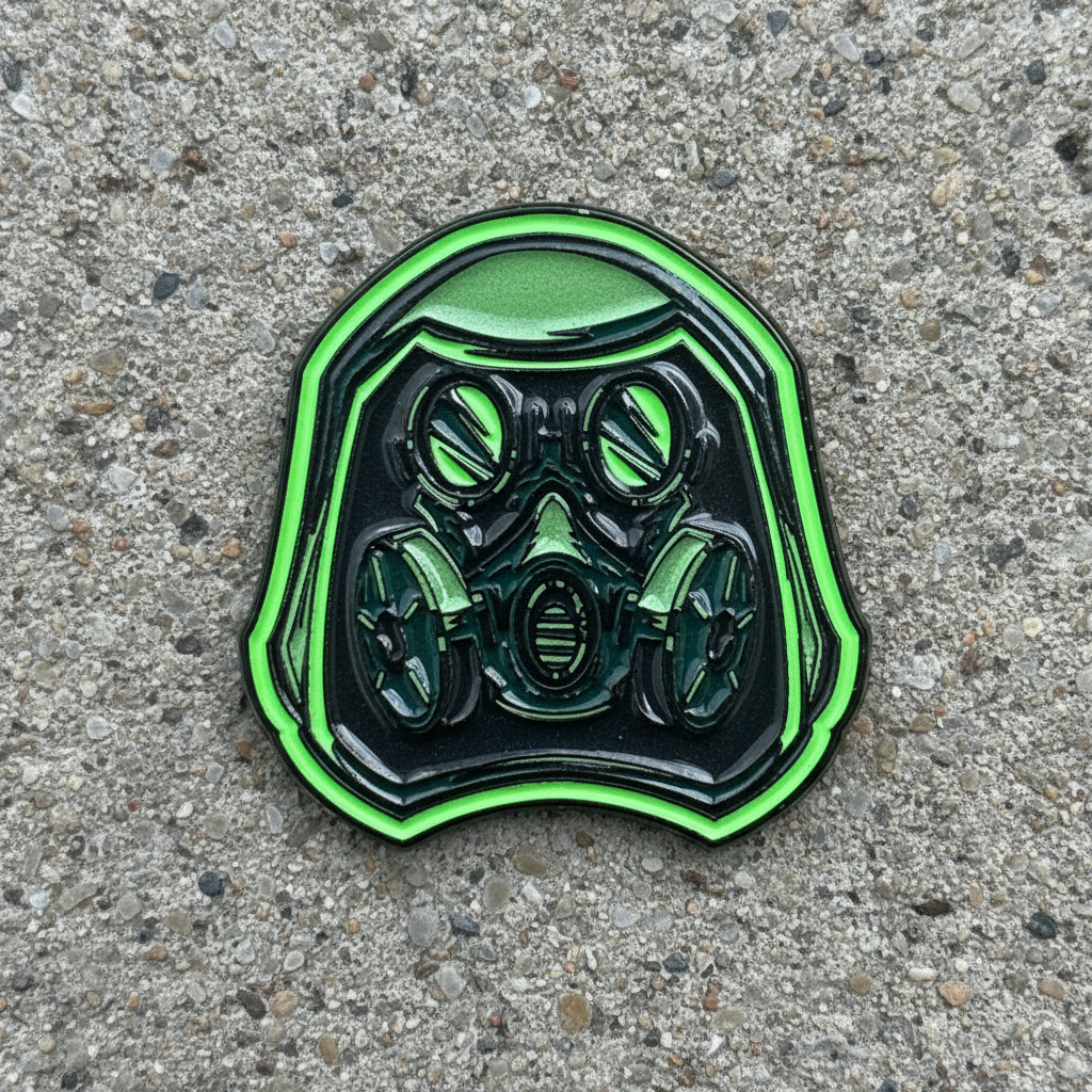 A green and black enamel pin shaped like a gas mask helmet, resting on a wooden surface.