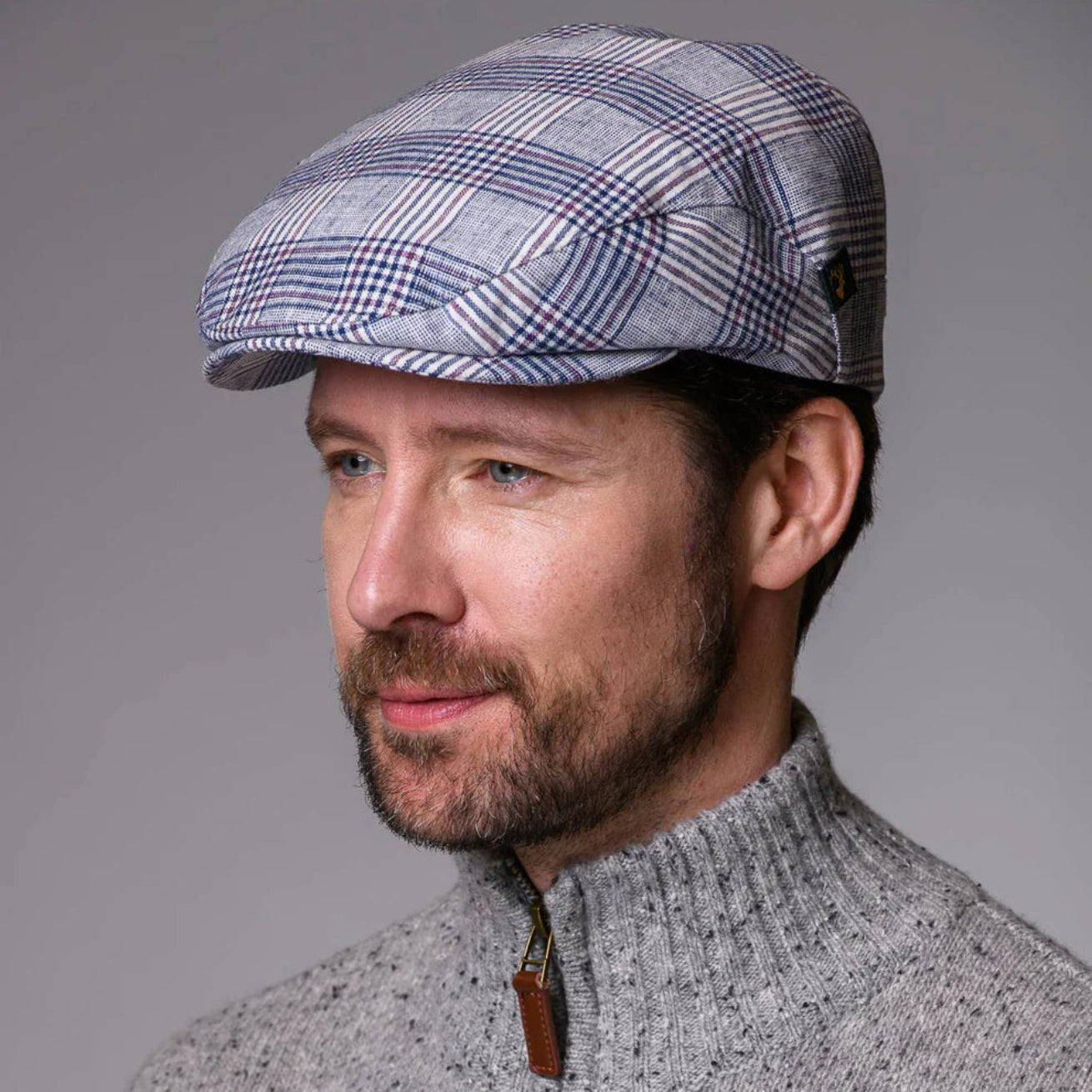 Man wearing a checkered cap and gray sweater against a gray background