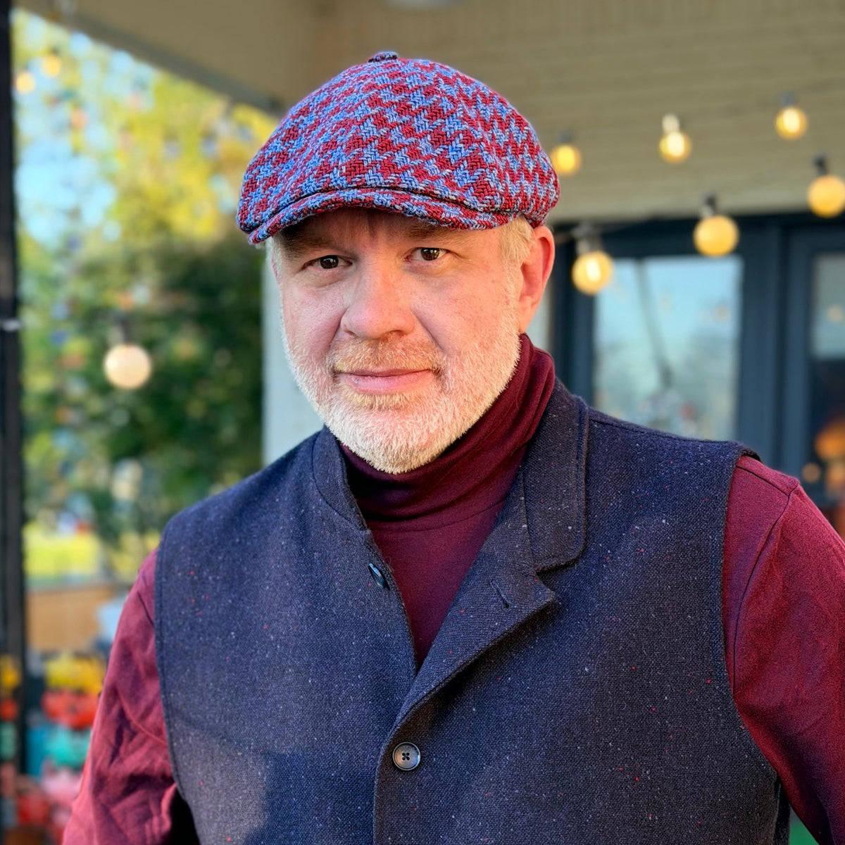 The Troubadour houndstooth newsboy cap worn with a burgundy turtleneck and dark vest, front view.