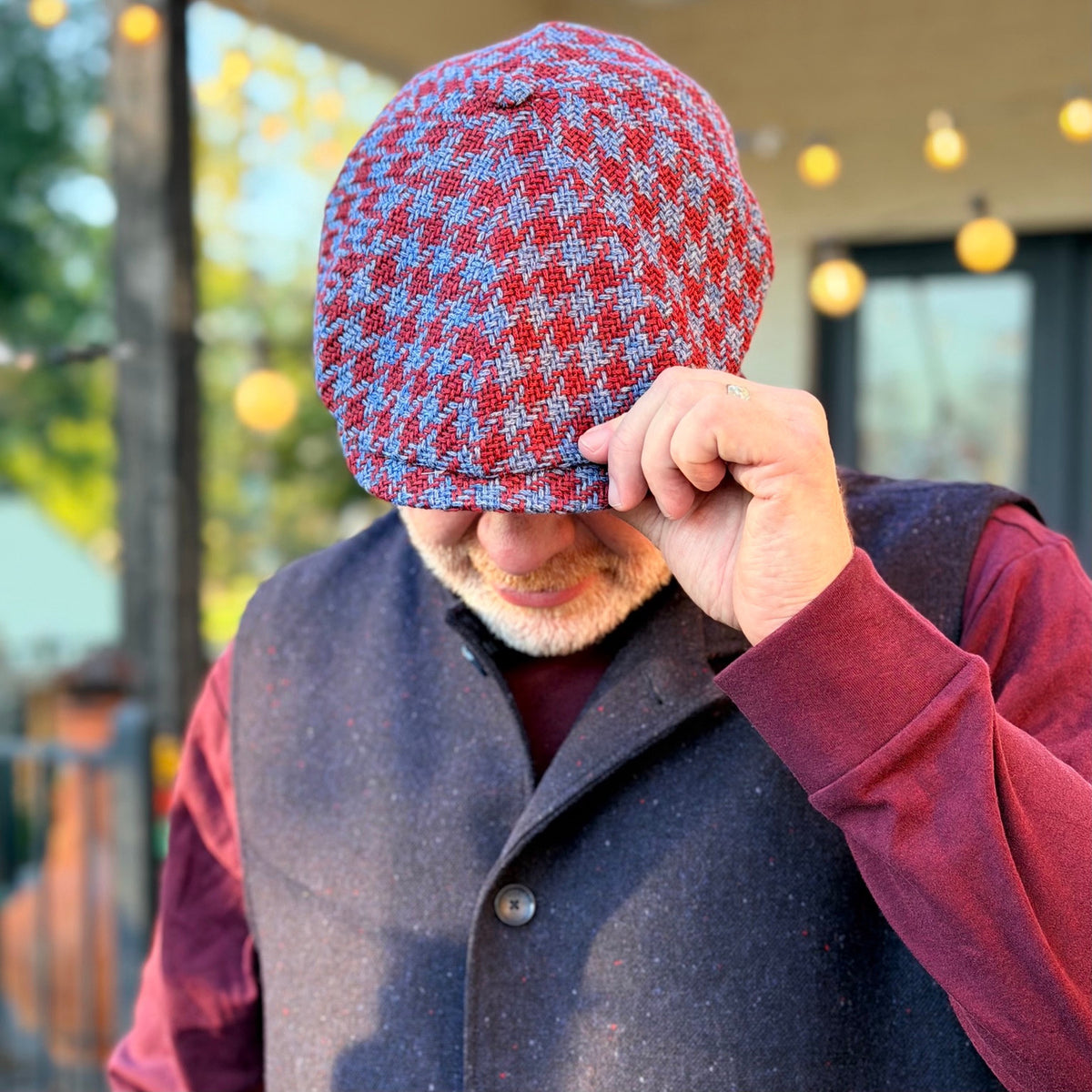 The Troubadour houndstooth newsboy cap being tipped forward, showing the patterned crown and brim.