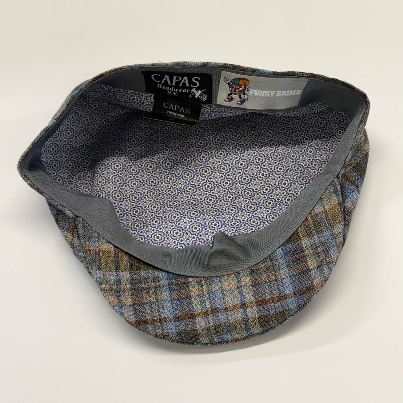 Plaid flat cap with patterned interior on a light gray background