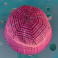 A pink and black patterned hexagonal kippah or skullcap photographed from above against a teal-blue background with circular cutouts.