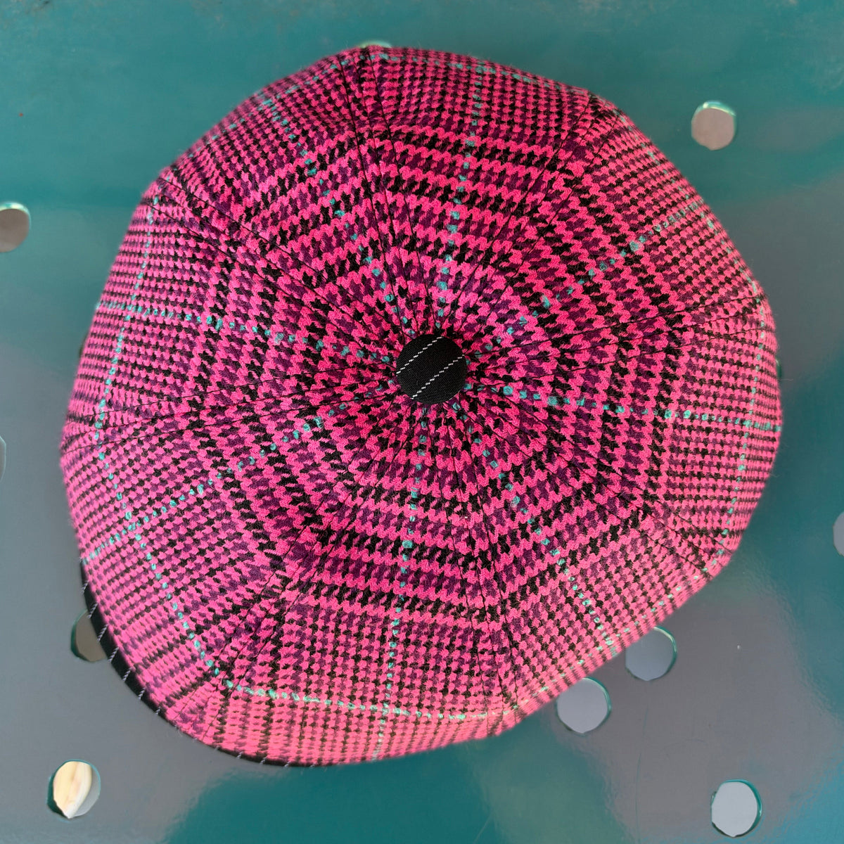 A pink and black patterned dome tent viewed from directly above, resting on a teal metal surface with circular cutouts.