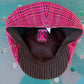 A pink and black patterned flat cap with a brown pinstriped brim, photographed from the inside. The interior lining is brown, and a pink ribbon patch is visible on the inner crown.