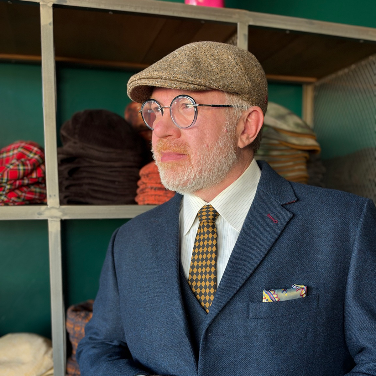 Model wearing the camel brown da Vinci Flat Cap by FunkyBrims with a navy suit, three-quarter view.